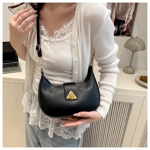 Detail of black hobo bag with gold triangular buckle worn on a model's shoulder