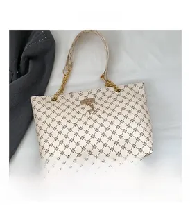 Detail of beige tote bag with retro diamond patterns, gold chain, and deer charm
