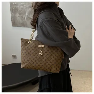 Detail view of brown tote bag with vintage pattern, gold chain strap and deer pendant