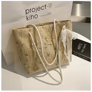 Detail of floral embroidery and white lace bow on beige woven straw tote bag