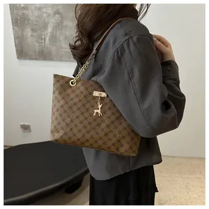 Detail of a brown tote bag with geometric patterns, gold chain strap and deer charm