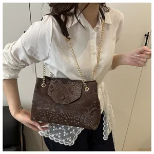 Gros plan du sac marron à motif serpent avec chaîne dorée sur une chemise en dentelle