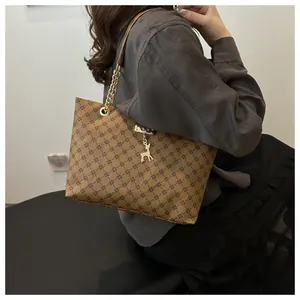 Macro detail of brown tote bag with cross pattern, gold chain handle and deer pendant