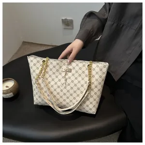 Detail of monogram tote bag featuring golden chain strap and a silver deer pendant