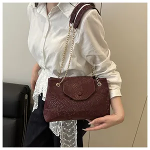 Detail of burgundy snakeskin embossed bag with gold chain strap on female model