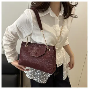 Détail d'un sac à bandoulière bordeaux gaufré avec chaîne dorée porté par un mannequin