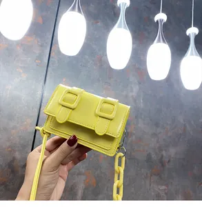 Detail of a bright yellow mini crossbody bag with thick plastic chain and metal buckles