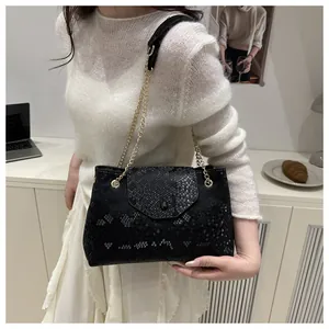 Détail du sac à main noir motif serpent avec bandoulière chaîne dorée sur l'épaule