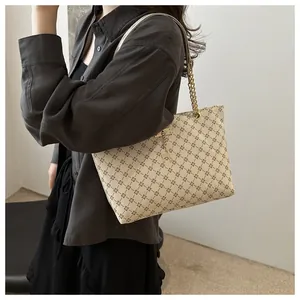 Detail view of beige tote bag with rhombus pattern and gold deer pendant on model's shoulder