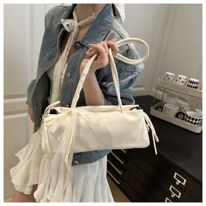 Detail of cream white leather underarm bag featuring a large lace bow and elegant strap