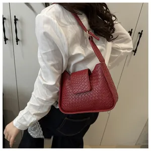 Détail de la texture tressée rouge foncé et de la bandoulière en cuir de ce sac sous l'aisselle