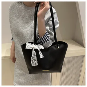 Detail of black tote bag with white lace bow and gold Fashion Bag logo on a shoulder strap