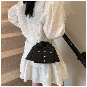 Detailed view of jacket-shaped black shoulder bag with metal chain on white dress