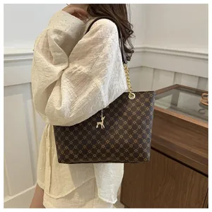 Detail of a brown tote bag with cross-pattern texture and gold deer charm on a model