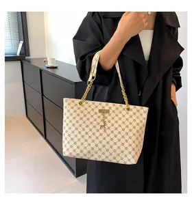 Detail of monogram tote bag featuring gold chain strap and deer pendant on model