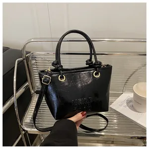 Detailed view of black patent leather bucket bag with embossed lettering and metal buckles