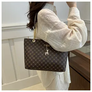 Detail of elegant brown tote bag with gold pattern and golden deer pendant on shoulder strap