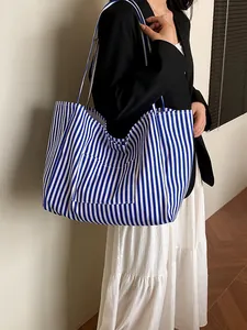 Large blue and white striped canvas tote bag shown on a model in a minimalist setting