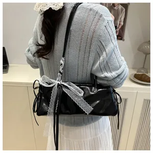 Detail of oil-wax leather baguette bag featuring a large white lace bow and black ribbons