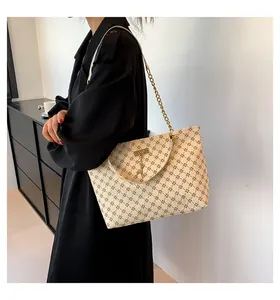 Detail of a beige monogram tote bag with gold chain strap worn by a model