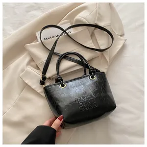 Detail of black glossy bucket bag featuring embossed letters and vintage cracked texture