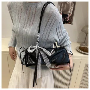 Close-up of black oil wax leather underarm bag with white lace bow and silk scarf