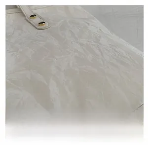 Detail of creamy white crinkled patent leather texture and gold rivet hardware on tote bag