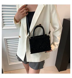 Detail of black tweed crossbody bag with textured fringe and round handle on white blazer
