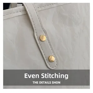 Close-up of fine stitching and gold rivet details on creamy white textured tote bag
