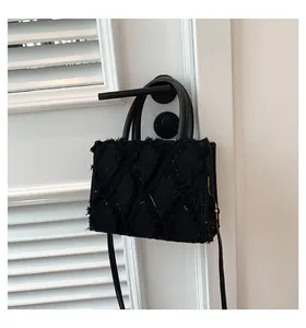 Detail of black tweed tote bag with fringe edges and quilted pattern on white door