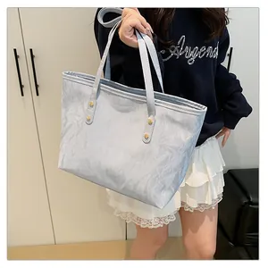 Close-up of light blue textured tote bag with elegant gold rivet strap details