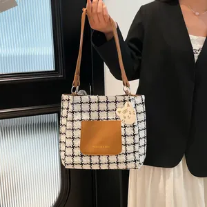 Fashion houndstooth tote bag with brown leather pocket and mascot charm held by model