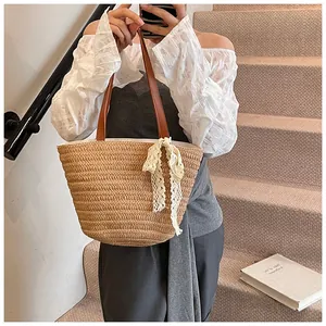 Detail of straw woven tote bag featuring beige lace bow and dark brown leather straps