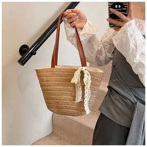 Detail of woven straw tote bag with brown leather handles and white lace bow decoration