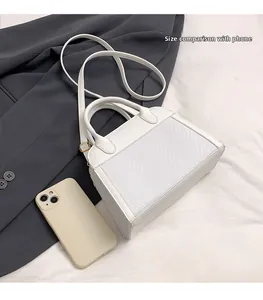 Compact white crossbody bag with woven texture and phone for size comparison