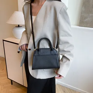 Detail of black crossbody pillow bag with woven texture and fashion slogan engraving