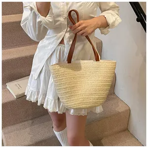 Close-up of the fine straw weave texture and brown leather handle on a beige tote bag