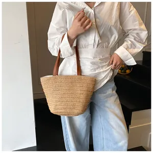 Close-up of woven straw texture and brown faux leather handles on a large summer tote bag