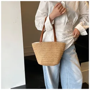 Close-up of woven straw tote bag featuring contrast dark brown leather handles