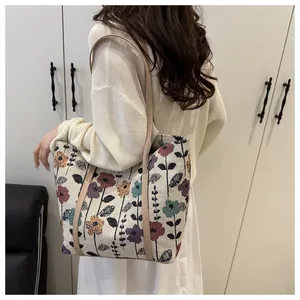 Detail view of floral embroidery on a large beige canvas tote bag with leather straps