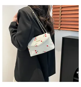 Detail of white corduroy shoulder bag featuring red cherry embroidery and gold chain strap