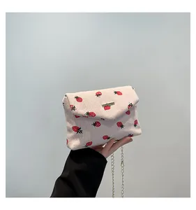Vue détaillée de la texture en velours côtelé à imprimé fraise et de la chaîne dorée du sac