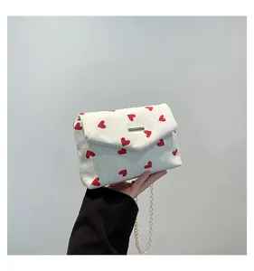 Gros plan du sac en velours côtelé blanc avec motifs cœurs rouges et chaîne dorée