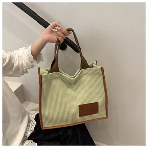 Detail of light green corduroy tote bag featuring a leather patch and brown woven handles
