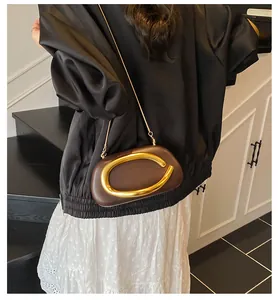 Detail of a brown oval clutch bag with a large gold metal buckle and elegant chain strap