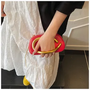 Chic red mini evening bag featuring a prominent gold C-shaped metal handle and chain strap