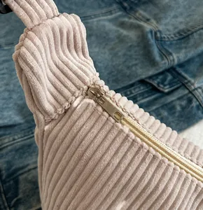 Detail of silver metal zipper on light pink corduroy shoulder bag against denim