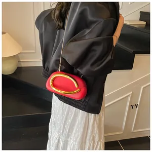Detail of red clutch bag with large oval gold handle and thin metal chain strap on model
