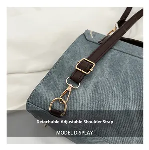 Détail de la bandoulière en cuir marron réglable sur un sac en denim bleu et crochets