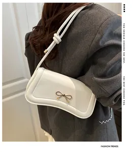 Detail of a white crossbody bag featuring a golden bow buckle and knotted rope strap